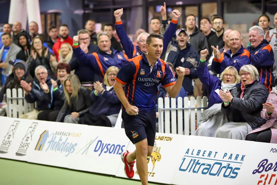Dandenong Club player celebrating a shot as the grandstand crowd cheers behind the fence
