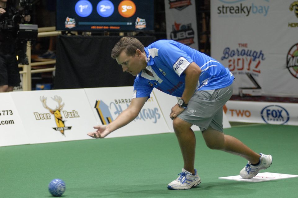 Bowler in a blue shirt delivering a bowl close to the green