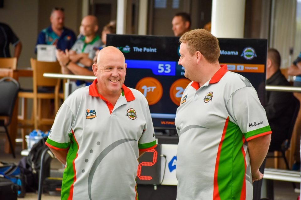Two Moama players in matching shirts sharing a smile beside the scoreboard