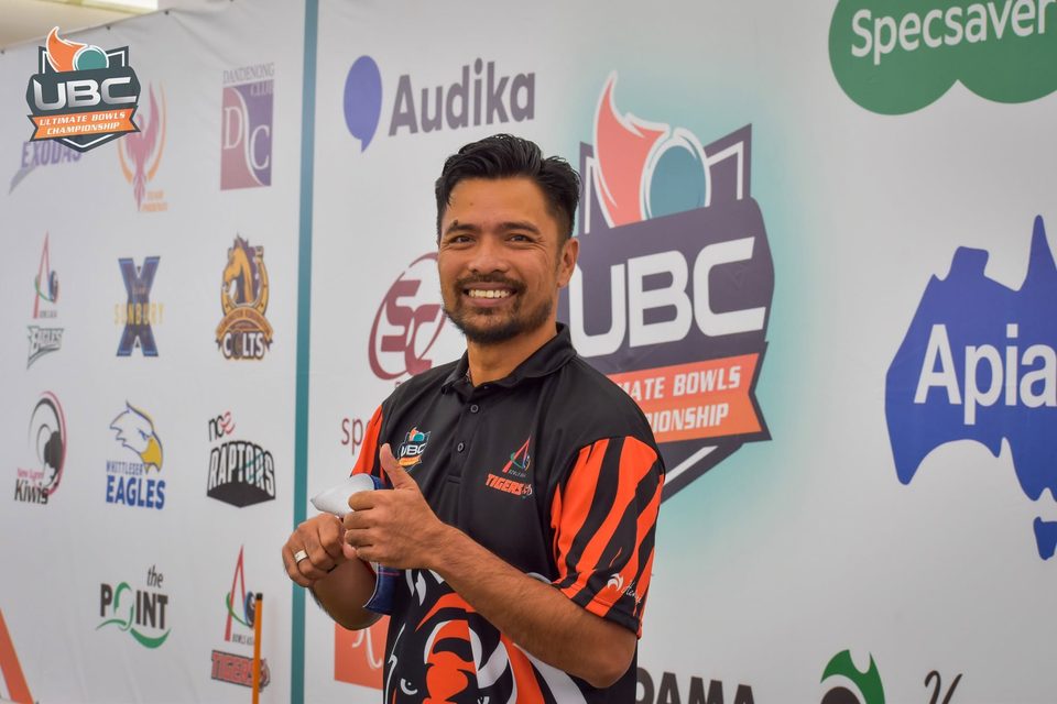 Bowls Asia Tigers player smiling with a thumbs up in front of the sponsor wall