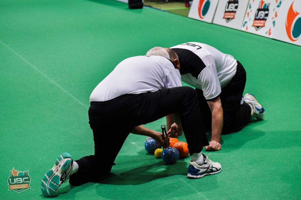 Two players kneeling on the green to measure the bowls around the jack