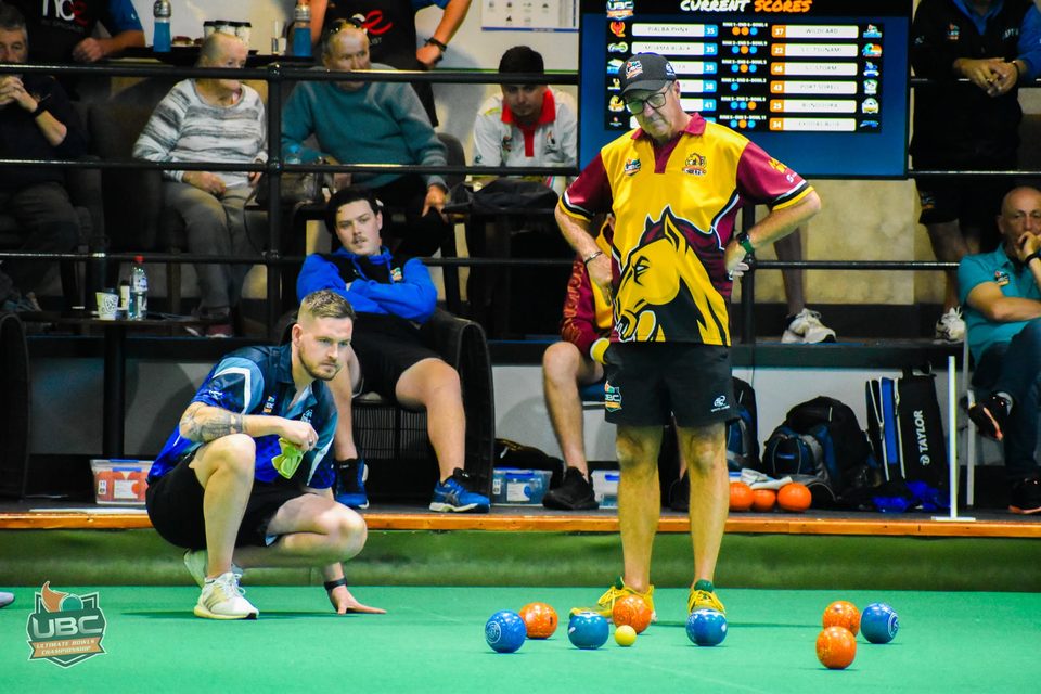 One player crouching and another standing to study the head of bowls