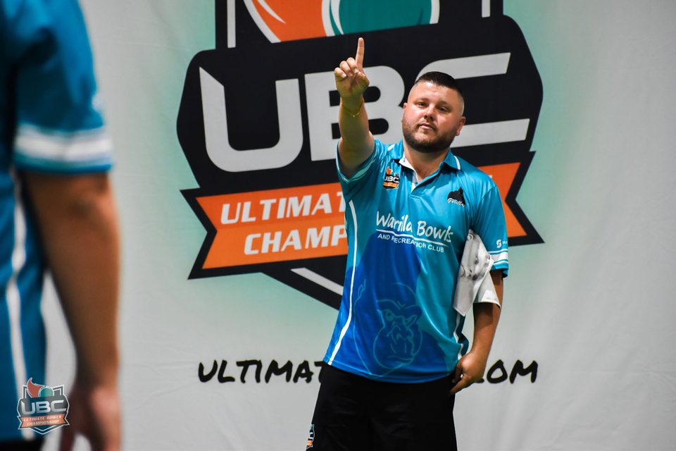 Warilla Bowls player pointing skyward in front of the UBC logo