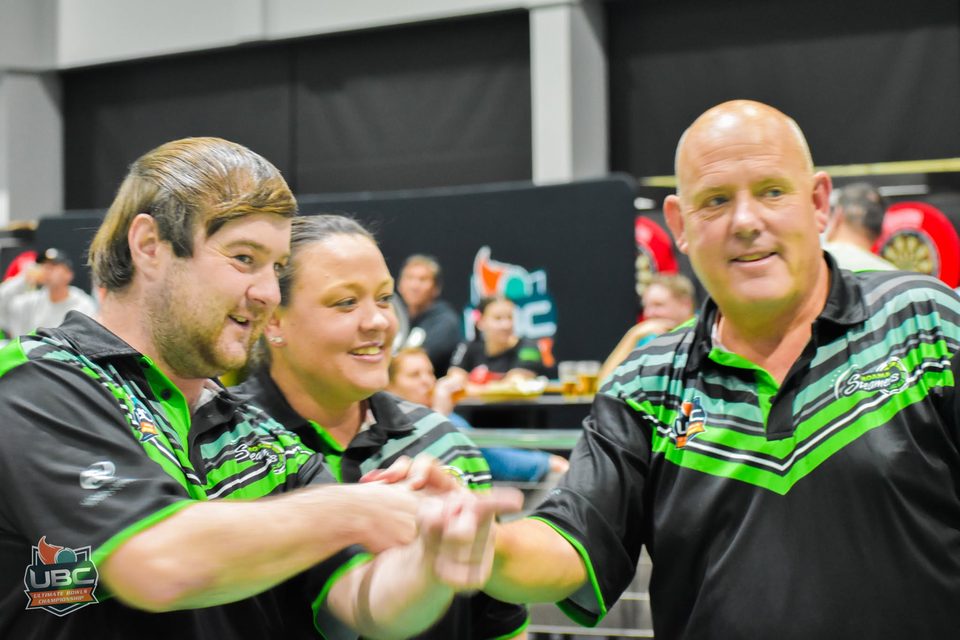 Three teammates in matching green and black shirts sharing a laugh