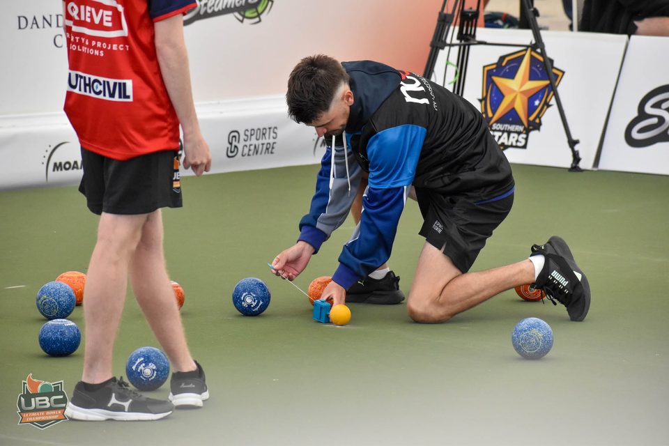 Player kneeling to measure between the bowls and the jack with a string